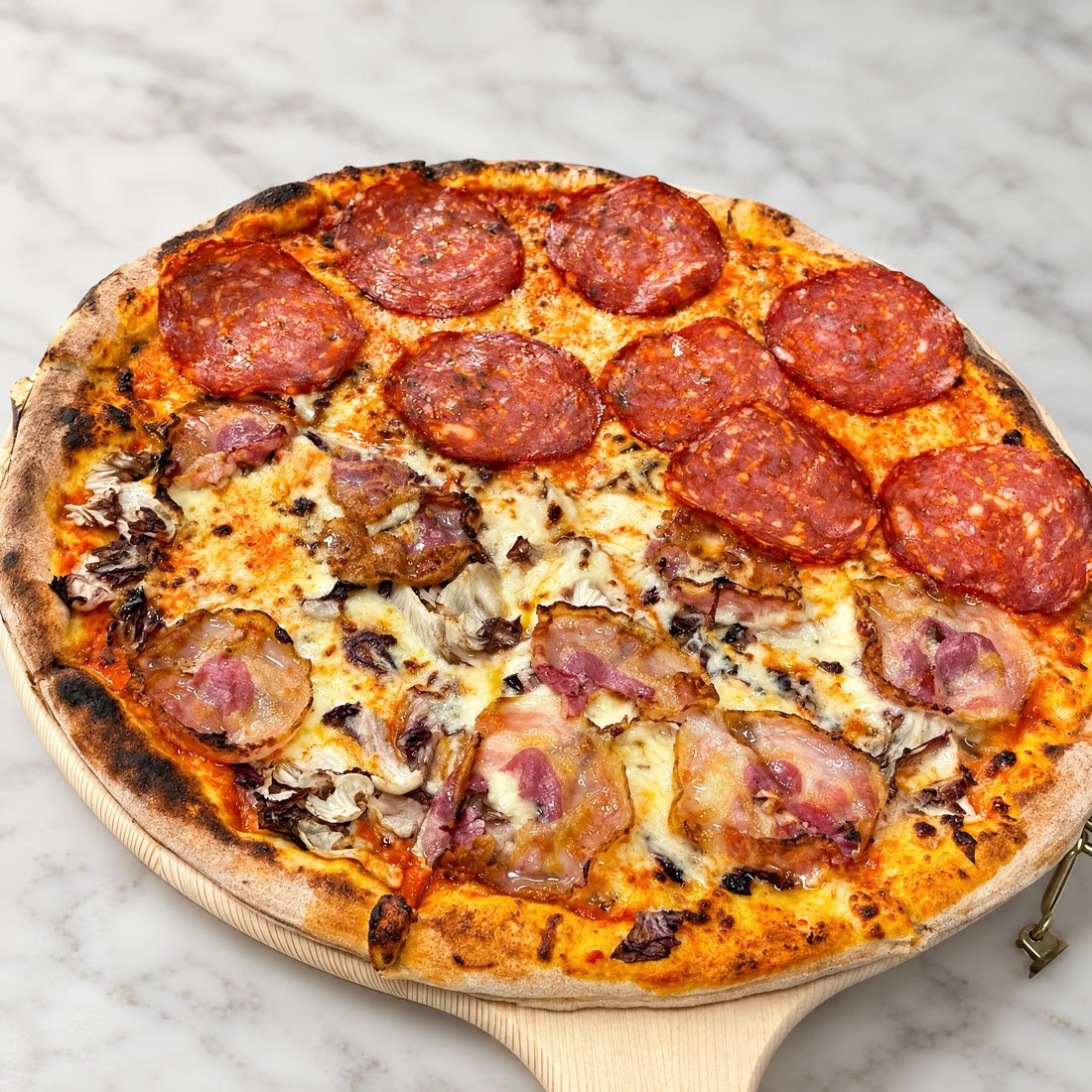 Pizza metà salame piccante e metà pancetta e radicchio, sulla pala di legno