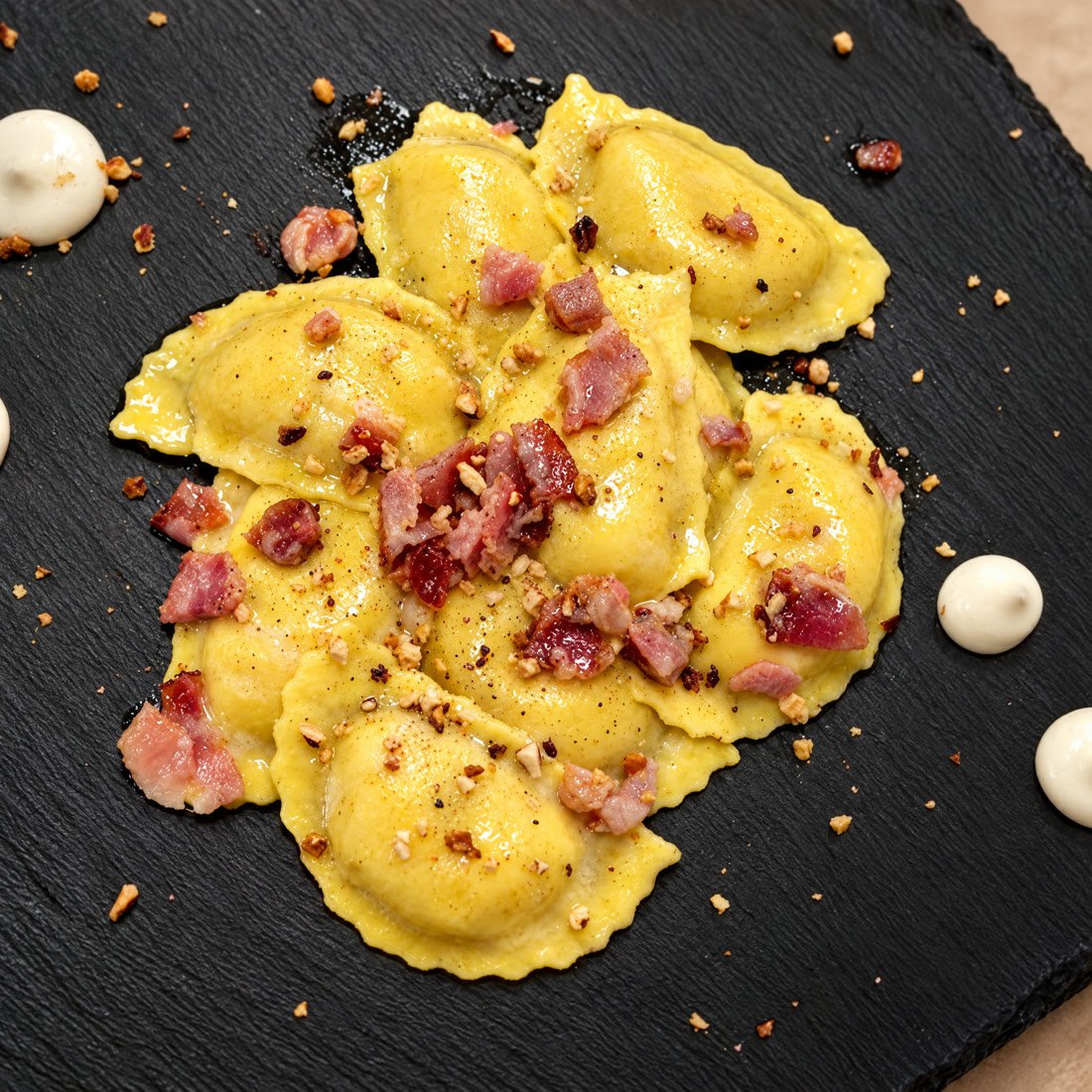 Mezze lunette cacio e pepe con burro e speck su un piatto di ardesia